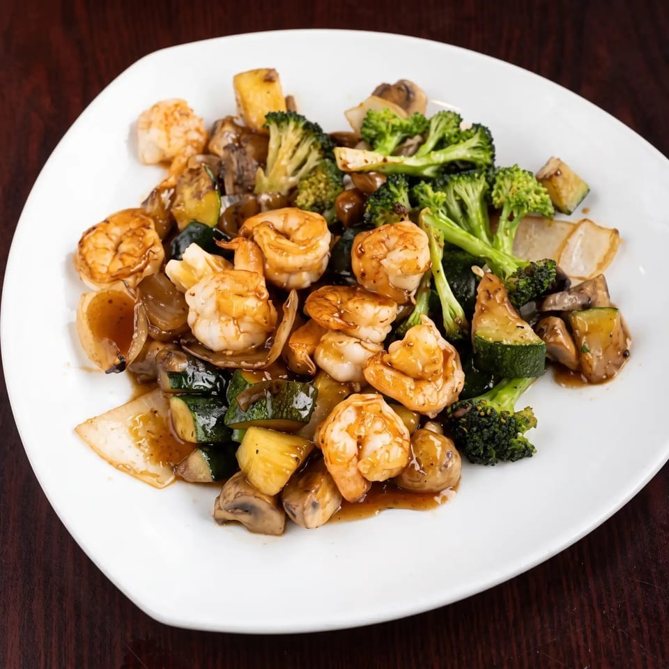 Shrimp and mixed vegetables, including broccoli, zucchini, mushrooms, and onions, on a white plate.