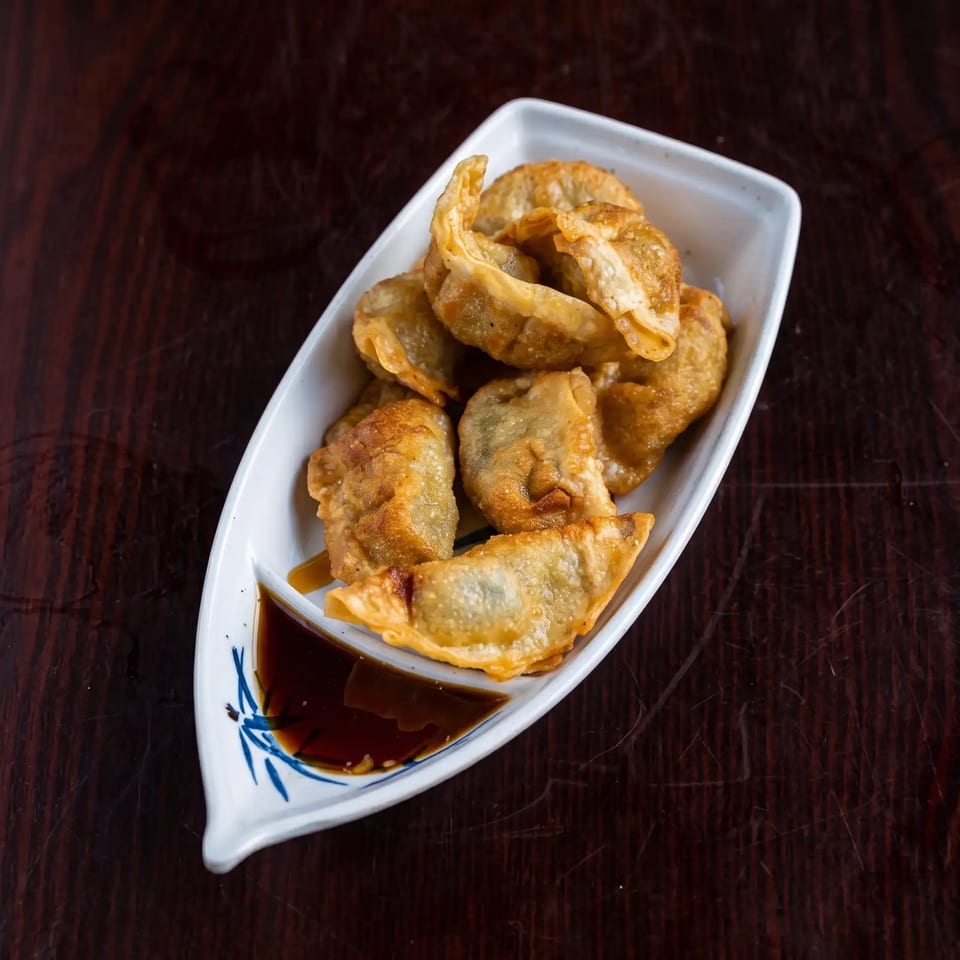 Golden-brown fried dumplings in a boat-shaped white dish with a side of soy sauce.