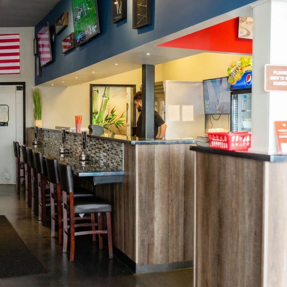 Interior of a casual restaurant with a bar, booths, and an American flag on the wall.