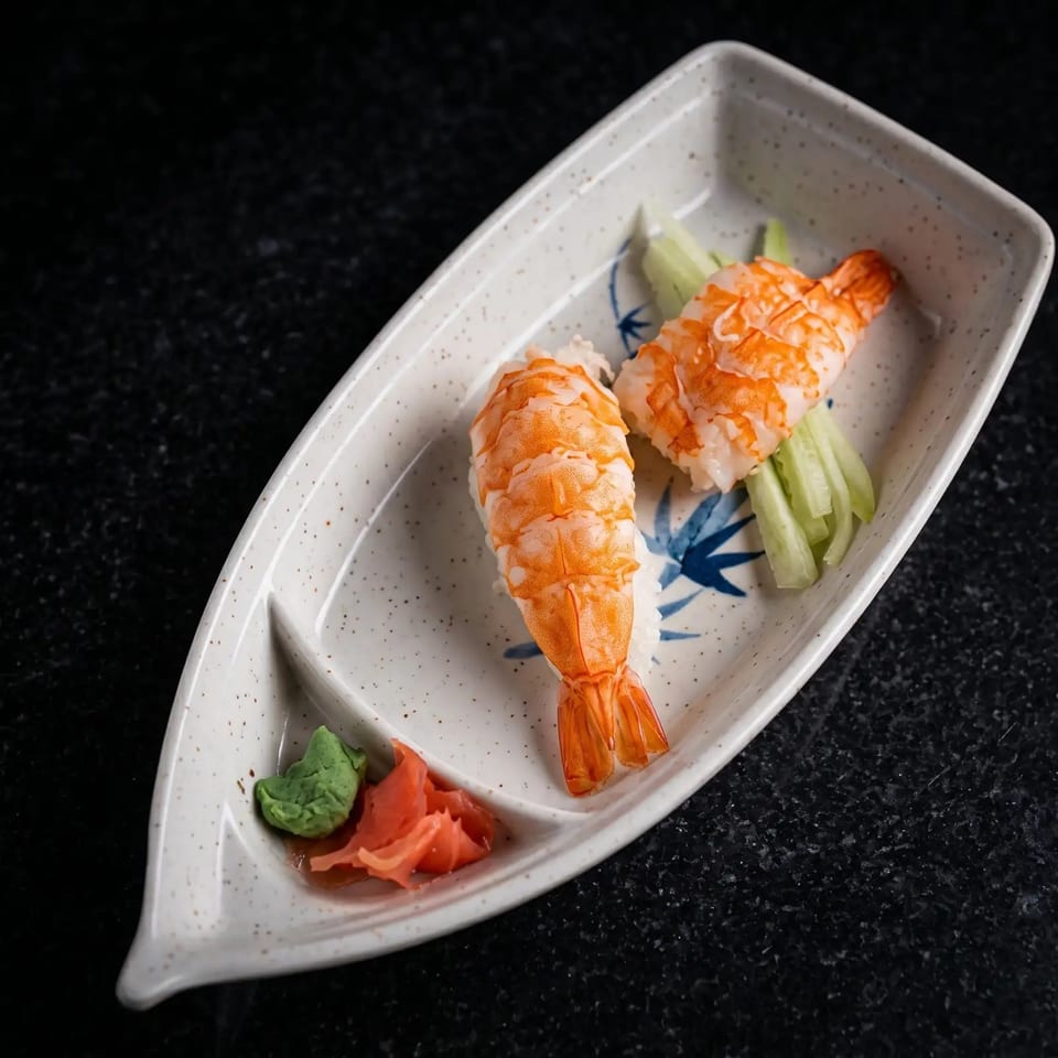 Two pieces of shrimp nigiri sushi with wasabi and pickled ginger on a boat-shaped plate.