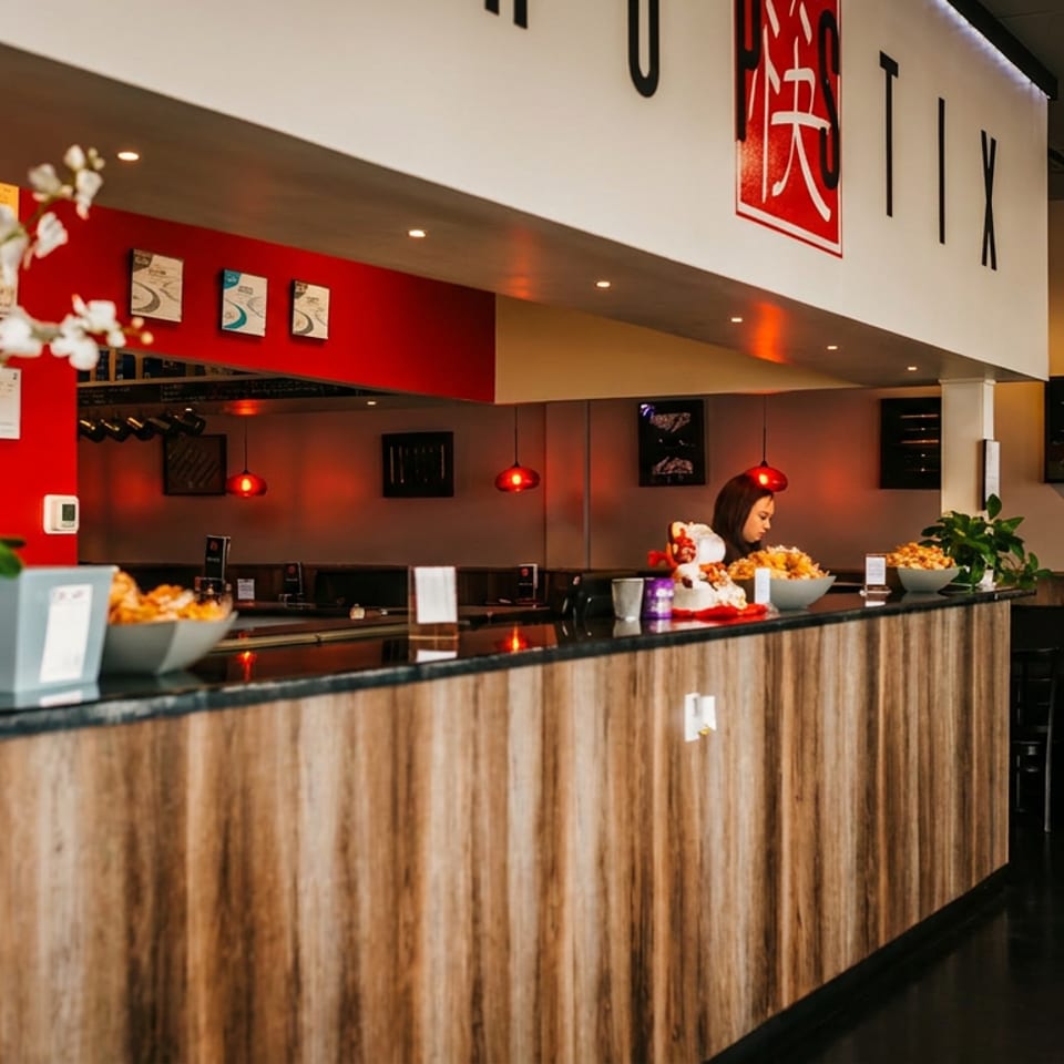 Restaurant interior with a long wooden counter, red accents, and a woman behind the counter.