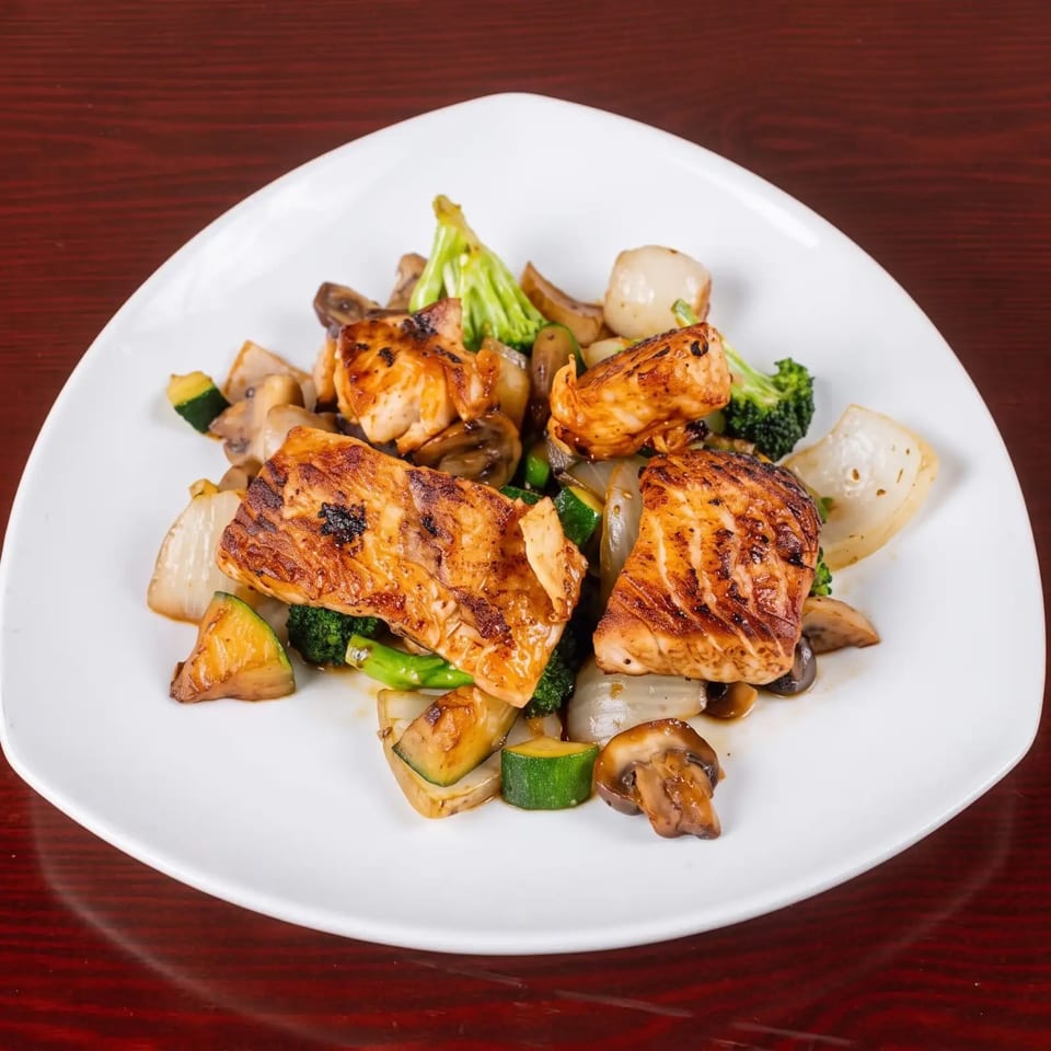 Grilled salmon fillets with broccoli, zucchini, mushrooms, and onions on a white plate.