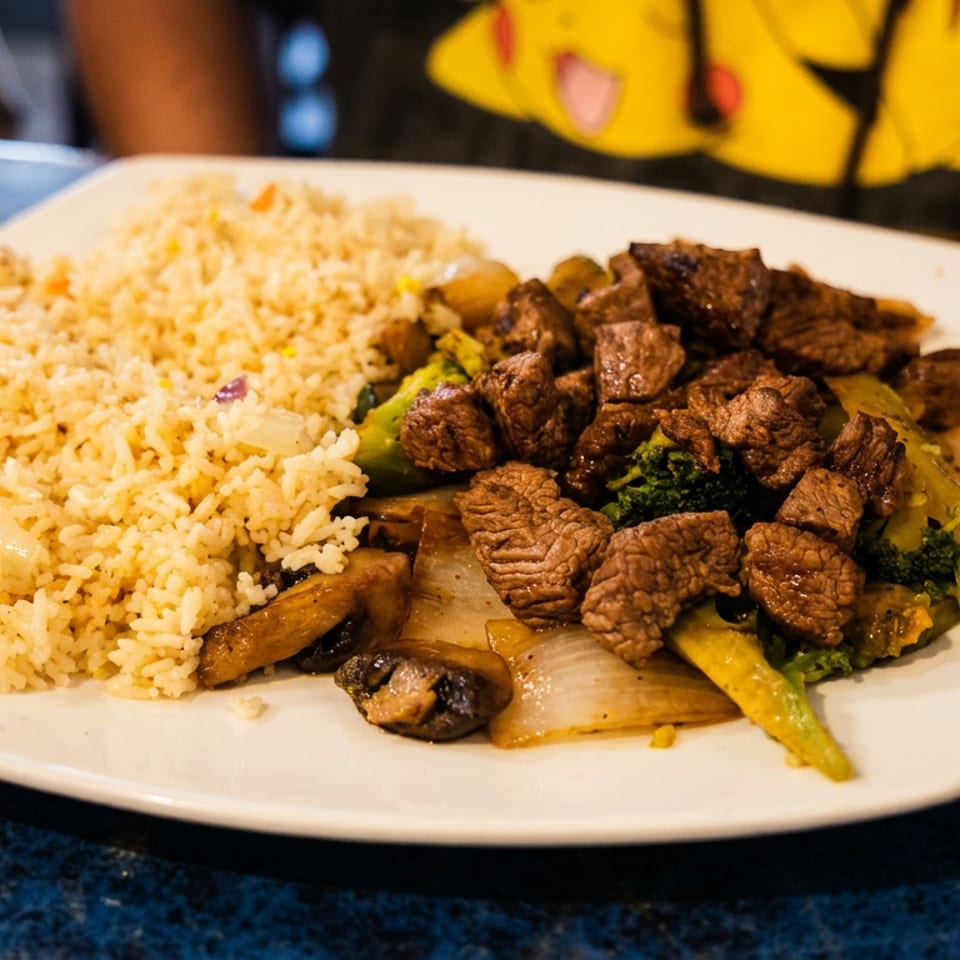 A plate of beef and broccoli stir-fry with onions and mushrooms, served with fried rice.