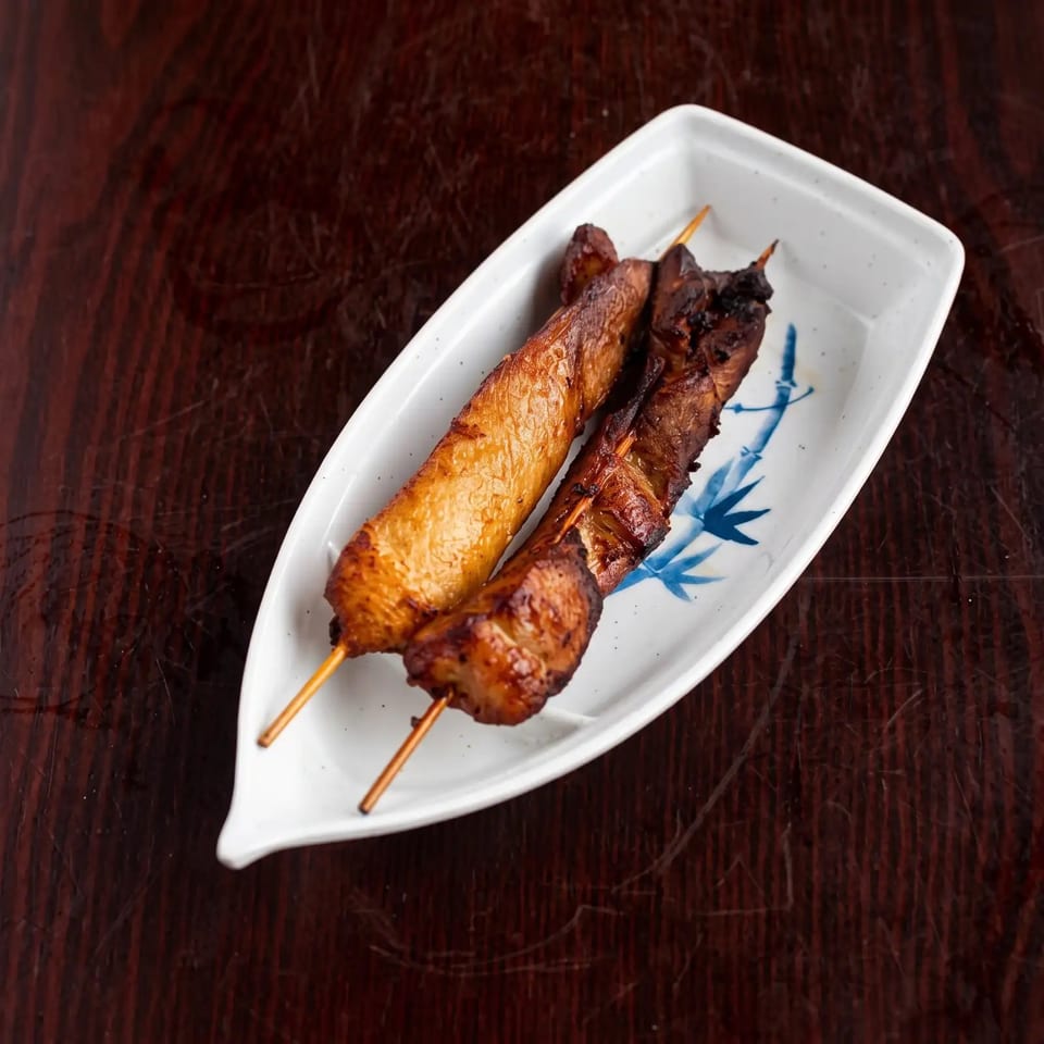 Two grilled chicken skewers on a white, boat-shaped plate with a blue bamboo design.