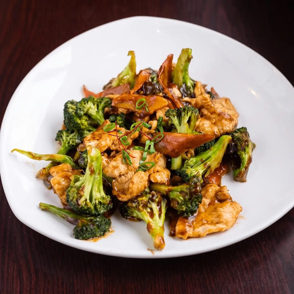 Chicken and broccoli stir-fry with mushrooms and carrots, garnished with scallions on a white plate.